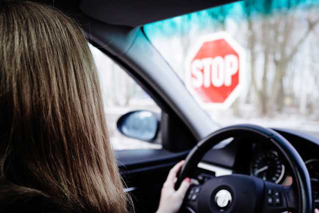 Frau im Auto steht vor einem Stoppschild