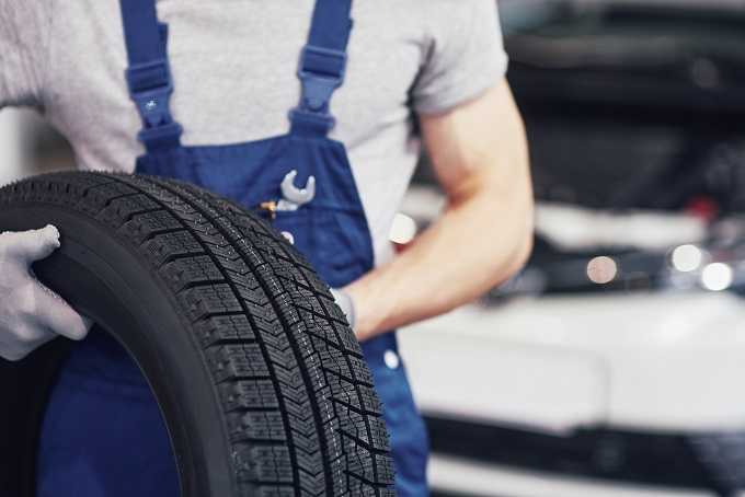 Mechaniker mit Reifen als Symbolbild für Reifenbezeichnung