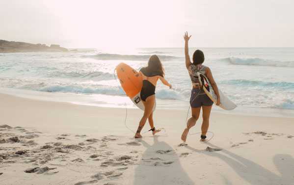Zwei Frauen mit Surfboards am Strand. 