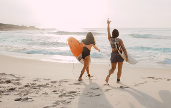 Zwei Frauen mit Surfboards am Strand.