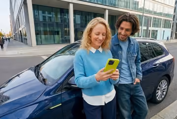 Frau und Mann stehen vor einem Auto und schauen gemeinsam auf ein Handy