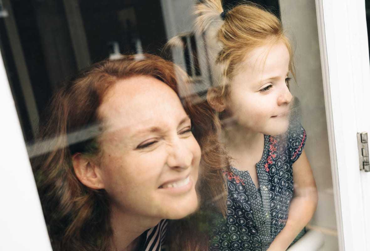 Mutter mit Tochter schauen aus einem Glasfenster